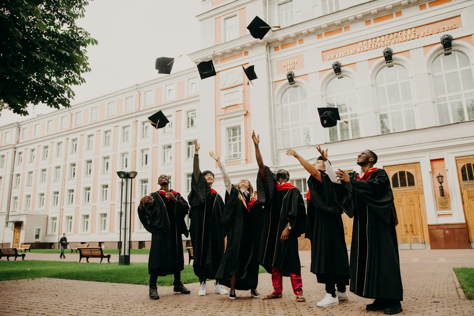 Graduates in gowns throwing their caps in front of a university building